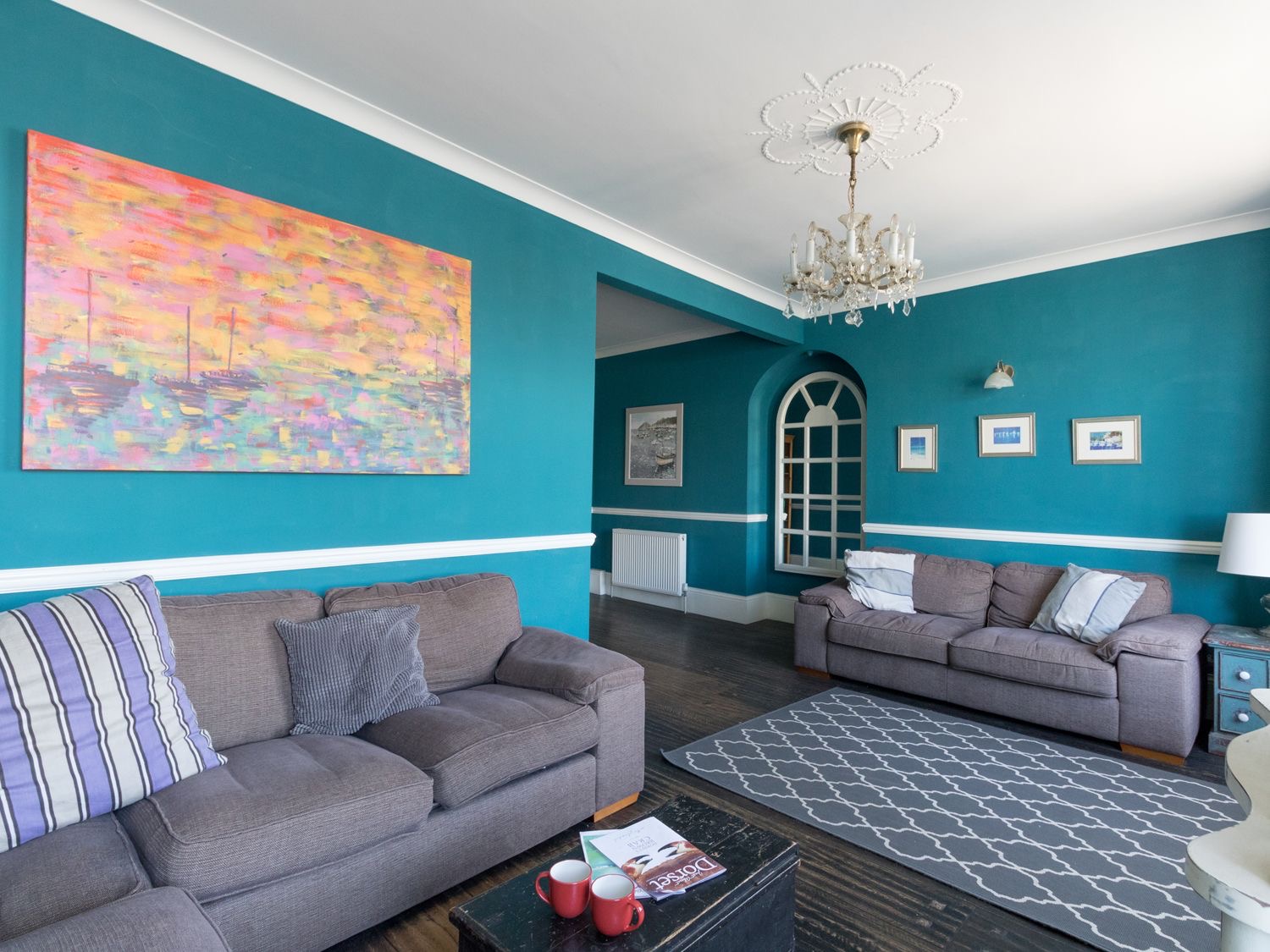 Sailor's Watch sitting room with teal walls, grey sofas and a large colourful painting