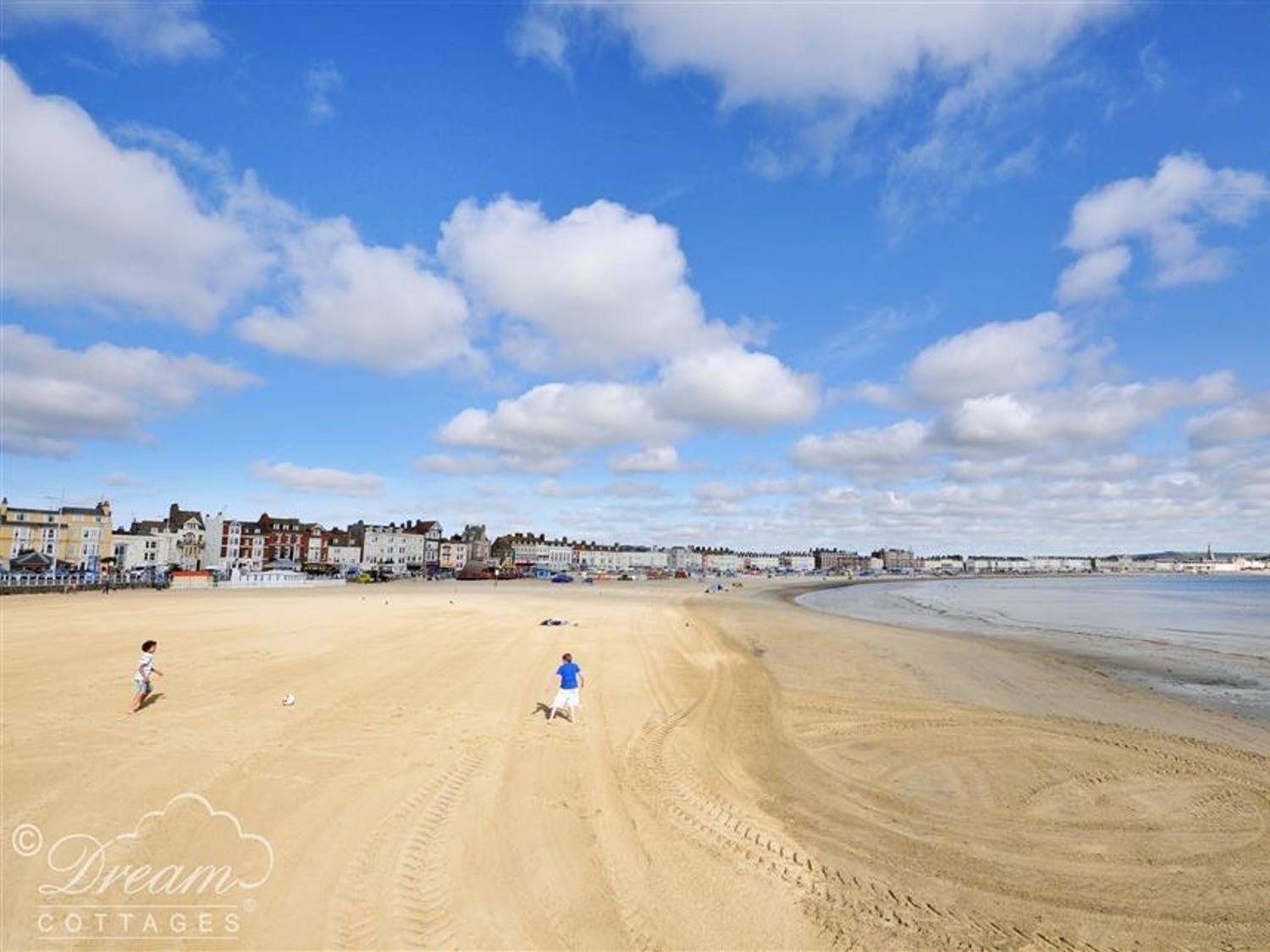 Weymouth's wide sandy beach at low tide under a blue sky