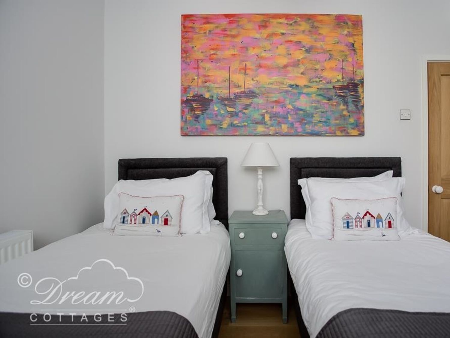 Twin bedroom at Waterside with beach-hut cushions and a colourful painting